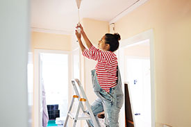 A young woman on a step ladder changes her light fixtures.